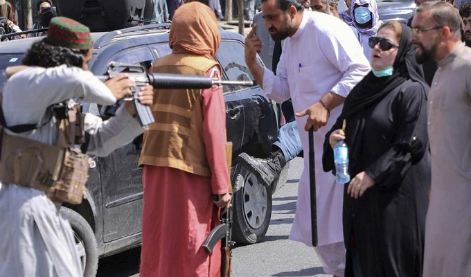তালেবান যোদ্ধার বন্দুকের সামনে দাঁড়িয়ে এক আফগান নারী।  ছবি সৌজন্যে রয়টার্স।